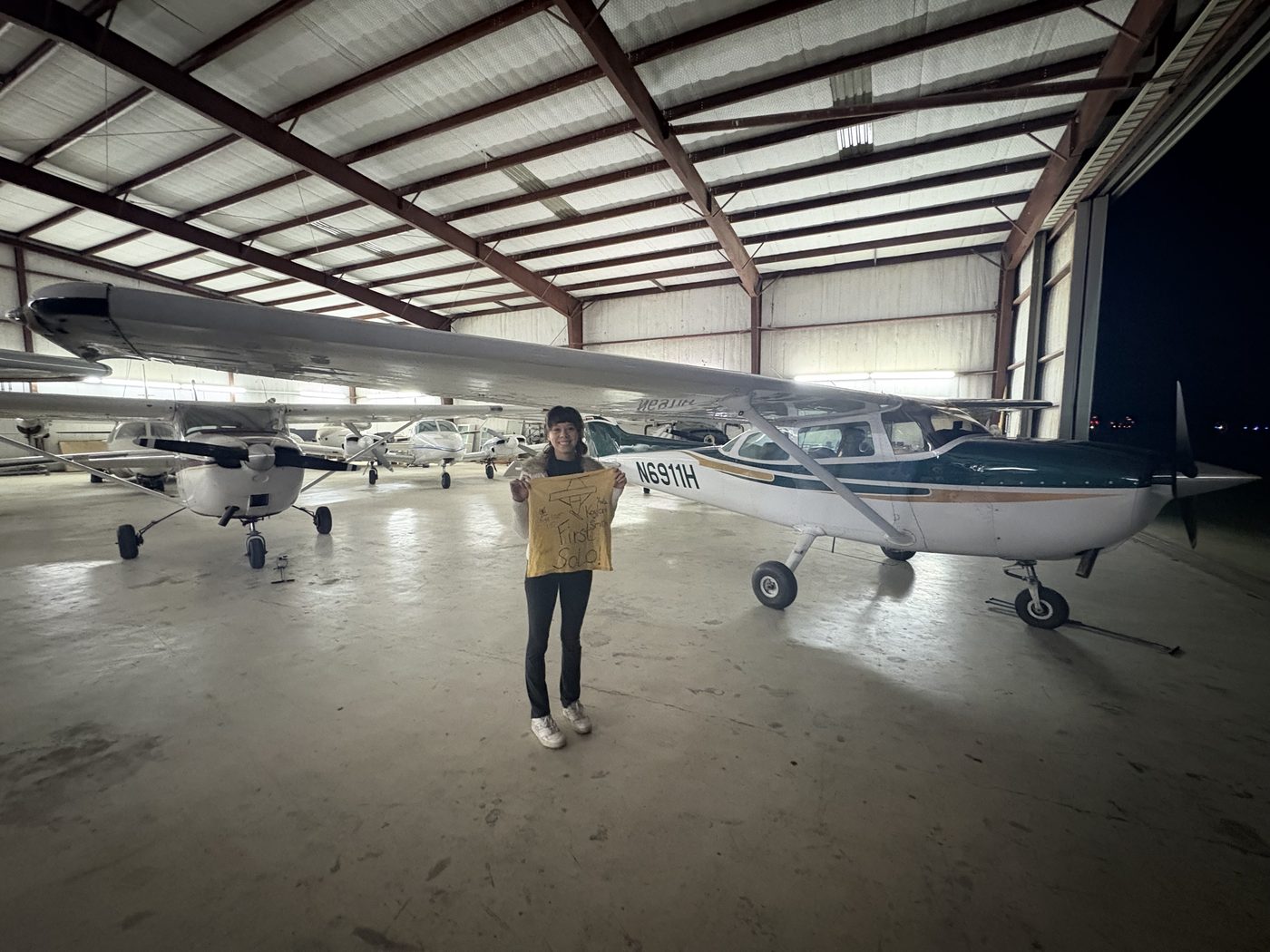 Student holding her first solo shirt in the hangar beside Cessna 172 N6911H